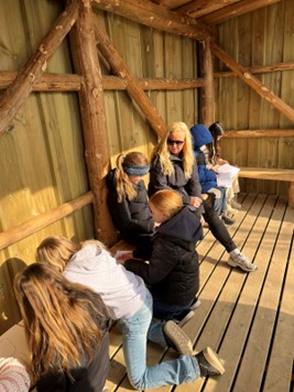 Learners in the outdoors, brainstorming their personal stories together in pairs. One learner is holding a small rock in their hand. A teacher is talking with one of the learners. A learner holds up a pen together with a cone they found while brainstorming. Photo: Marte Maurabakken/Climate Creativity.